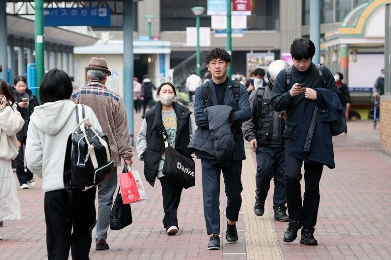 春のような陽気の下、コートなどを脱いで歩く人たち＝１５日午後３時３２分、ＪＲ岡山駅東口広場