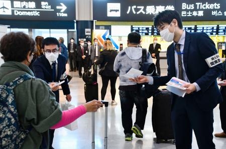 　旅行客（左端）に「白タク」への注意を喚起するチラシを配る国交省の職員＝１日午前、成田空港