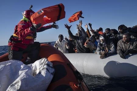 　リビア沖の地中海で、支援者からライフジャケットを受け取るゴムボートに乗ったアフリカからの避難民たち＝２０２２年１月（ＡＰ＝共同）