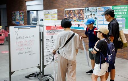 　台風６号の影響による列車の運休を伝える案内板を見る家族＝９日午後、ＪＲ長崎駅