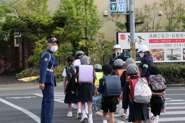 登校中の児童を誘導する警察官ら＝１５日午前７時５２分、岡山市立大野小近くの交差点