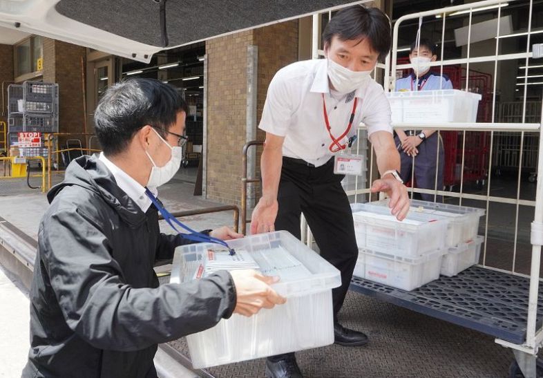 岡山中央郵便局に４回目接種券を届ける岡山市職員（左）