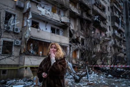 　２０２２年２月、ウクライナの首都キーウで、砲弾を受けた自宅脇に立つ女性（ＡＰ＝共同）