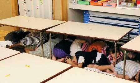 　ミサイル避難訓練で、机の下に隠れる園児たち＝７日午前、石川県かほく市