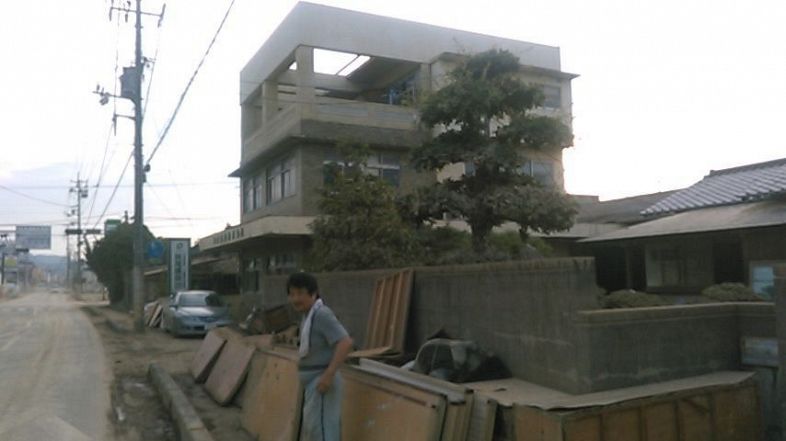 被災直後の妹尾さん。並べてられているのは水に浸かった家具。右側には解体前の自宅も見える＝２０１８年７月１３日（筆者撮影）