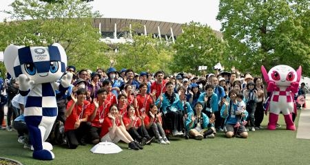　東京五輪の開幕から２年となり、イベントに集まった大会ボランティアの経験者やマスコット。後方は国立競技場＝２３日午前、東京都新宿区