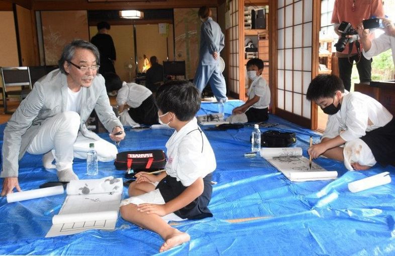真庭市で開かれた武藤さん（左）による墨絵の「寺子屋」。小中学生８人がオリジナルの絵巻物を仕上げた＝２５日