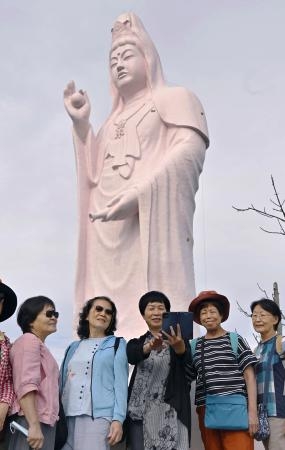 　ピンク色の「仙台大観音」を背に写真を撮る外国人観光客＝２５日午前、仙台市
