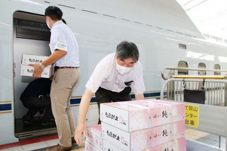 清水白桃の箱を新幹線に運び込むスタッフ＝３日午前７時２分、ＪＲ岡山駅