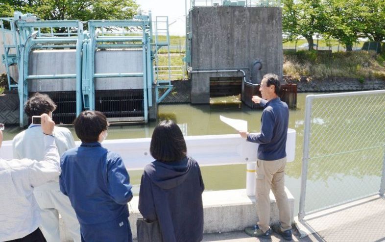 ポンプ場で実験内容を説明する平井代表（右端）。左奥がごみ回収機＝１１日、岡山市中区海吉