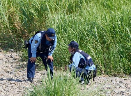 　小学生３人が川に流された現場付近を調べる警察官＝２１日午後３時１８分、福岡県宮若市