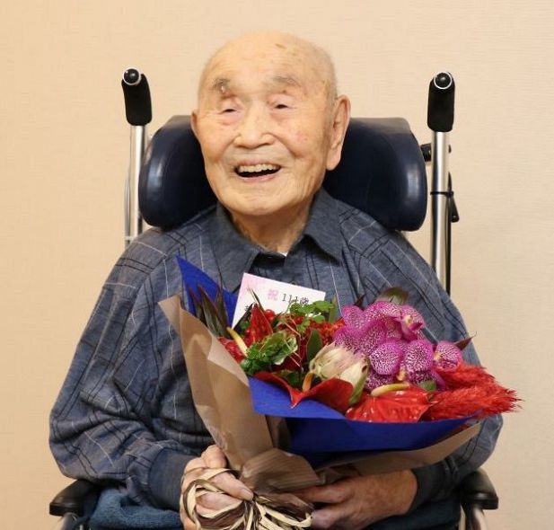 贈られた花束を手に笑顔を見せる、国内男性で最高齢となった中村さん