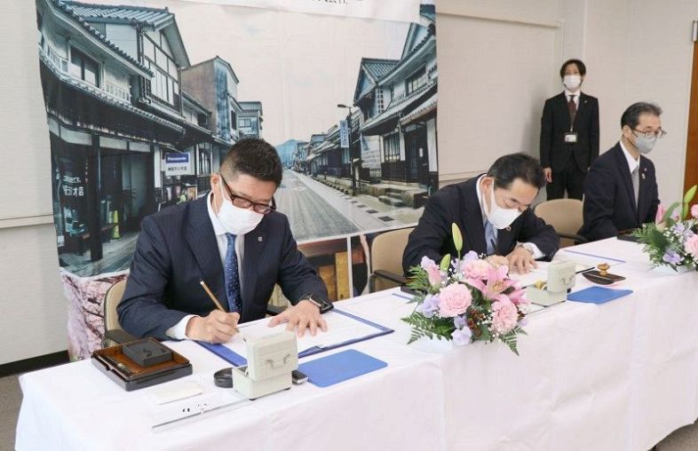 協定書に署名する（左から）大西社長と山岡町長