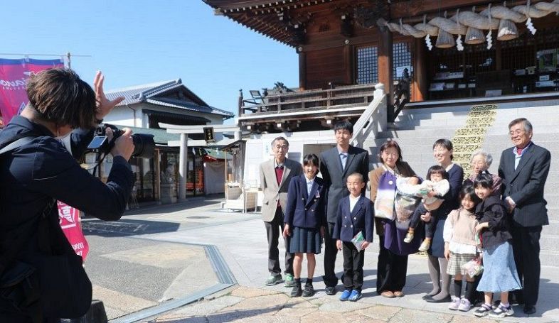小分坂さん（左）に集合写真を撮ってもらう家族＝３月５日、沖田神社