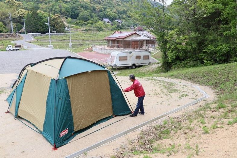 キャンプ区画にテントを設置する長屋事務局長。キャンピングトレーラー（中央）などにも宿泊できる