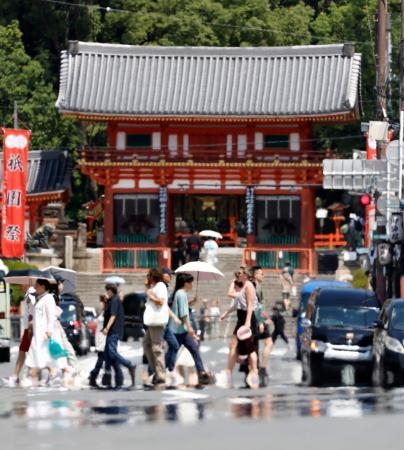 　厳しい暑さの中、京都・八坂神社の前を歩く人たち。熱くなった道路には「逃げ水」が見られた＝２７日午後
