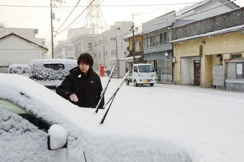 車に降り積もった雪を落とす住民＝２２日午前７時４３分、新見市高尾