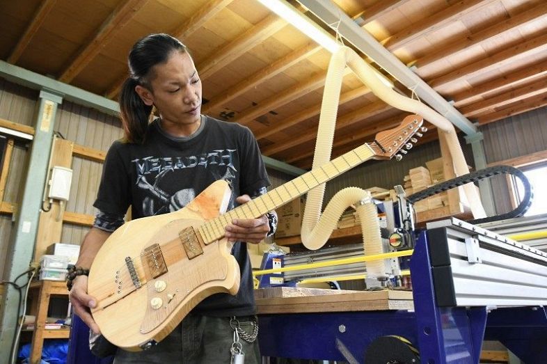 新庄村産ヒノキのエレキギター第１号を手にする香山さん。量産化に向けＣＦで支援を募り始めた